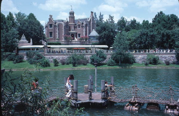 Barrel bridge to Tom Sawyer Island attraction with the Haunted Mansion in the background at the Magic Kingdom - Orlando, Florida. Keep reading for Disney World Haunted Mansion secrets and facts.