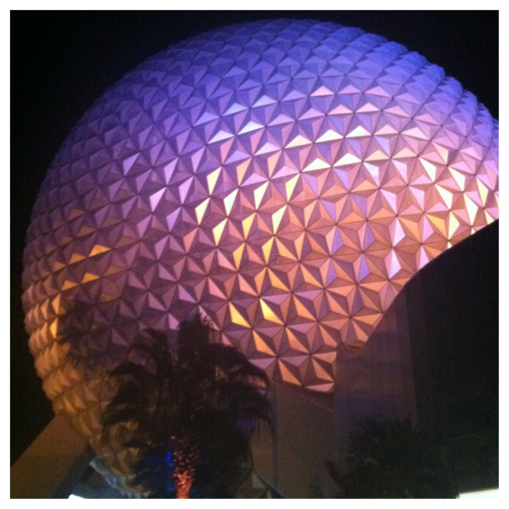 Les Chef de France Epcot at Night with Spaceship Earth lit in shades of purples and pinks.
