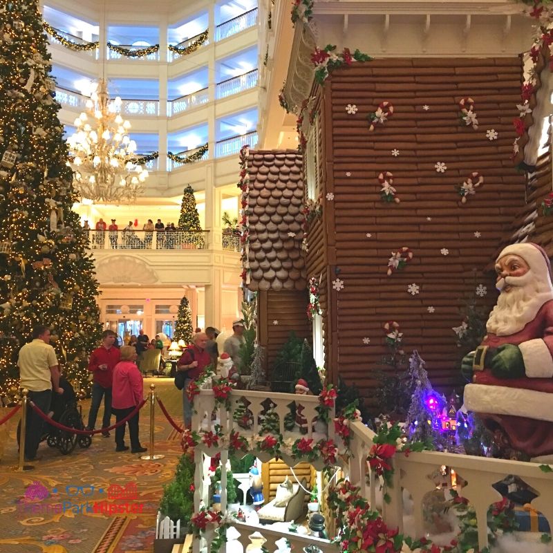 Disney Grand Floridian Gingerbread House Display with Santa on the Porch and Christmas Tree in the Background. Keep reading to get your perfect Disney Resort Christmas Decorations Tour!