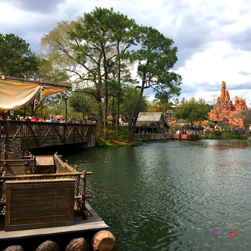 Tom Sawyer Island at Magic Kingdom with raft on water and Big Thunder Mountain Railroad in the background. Disney Secrets.
