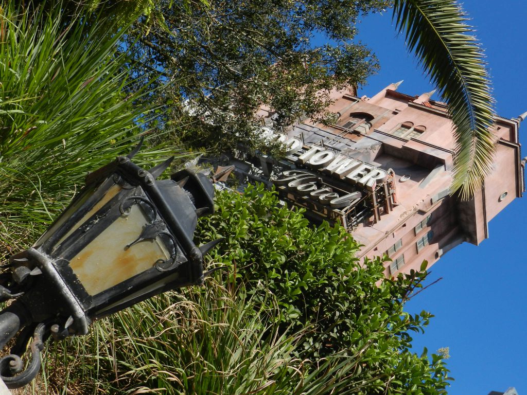 Erie outdated lamppost and overgrown palms outside the façade of The Hollywood Tower Hotel, home of The Twilight Zone Tower of Terror at Disney World Hollywood Studios. If you want to take deep dive into Twilight Zone Tower of Terror: Secrets REVEALED, keep reading!