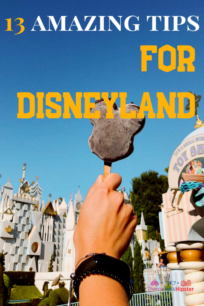 13 Amazing Tips for Disneyland with delicious chocolate Mickey Mouse Ice cream bar with it's a small world ride in the background on a sunny California day.