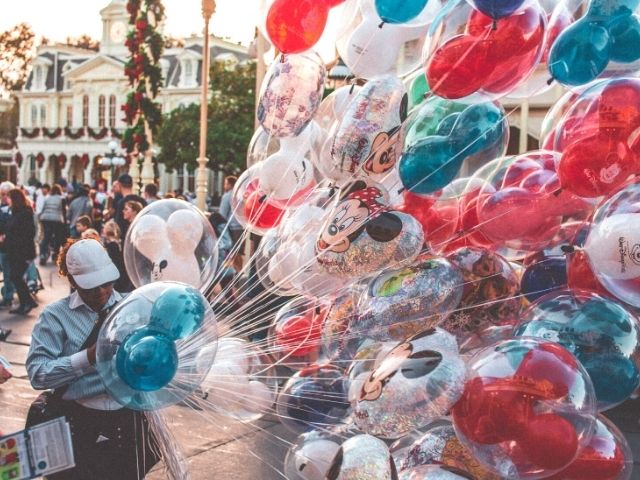 Disney Cast Member holding Mickey Mouse and Minnie Mouse balloons. Keep reading for the hidden best kept secrets of Disneyland!