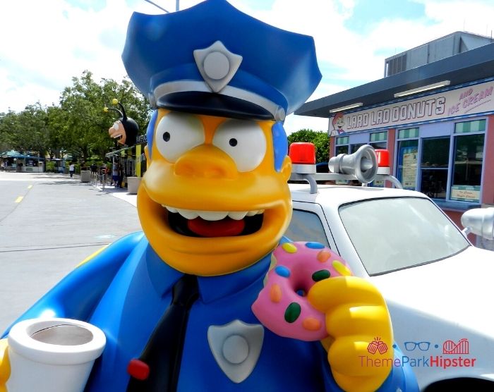 Chief Wiggum from the Simpsons eating a big pink donut. Keep reading to learn about the cheap, best food at Universal Studios Orlando, Florida.