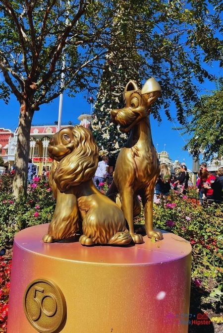 Lady and the Tramp Gold Statue with Christmas Tree in the Background at the Magic Kingdom. Keep reading to learn about the best things to do at Disney World for Christmas.