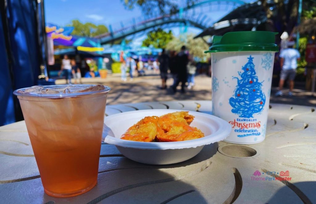 SeaWorld Christmas Celebration Red Holiday Cocktail and Shrimp in front of Mako Roller Coaster. Keep reading to learn about the 2024 SeaWorld Annual Pass and Pass Member Perks and Benefits.