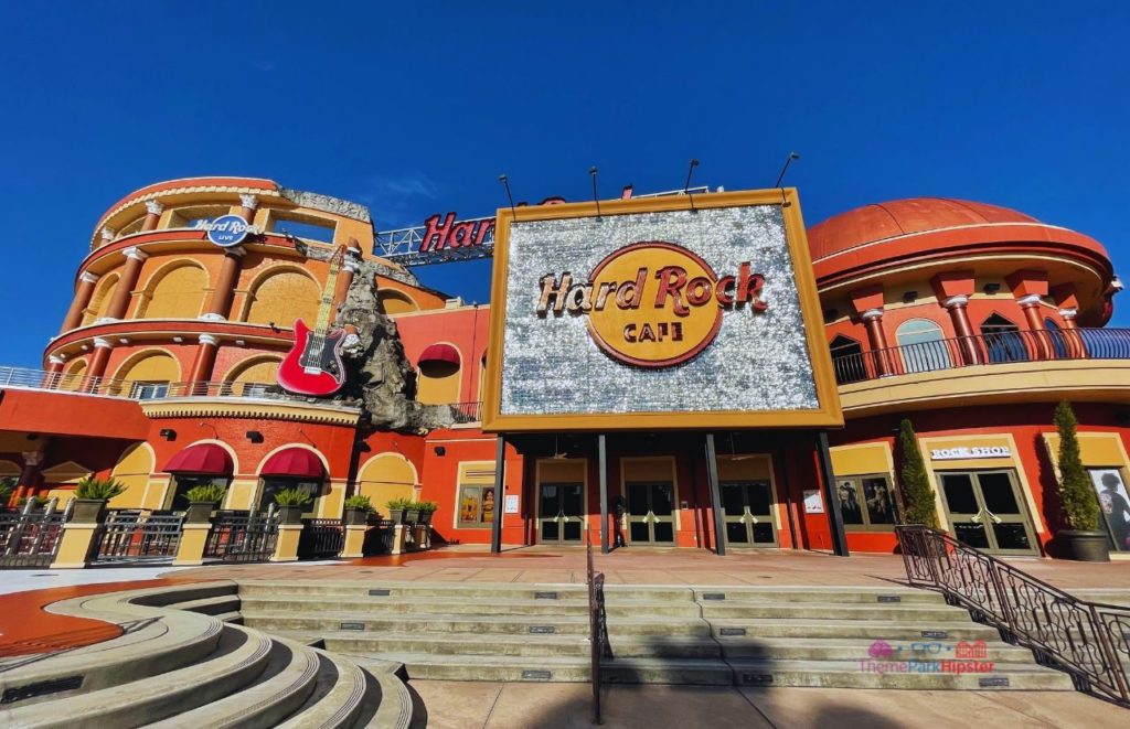 Steps leading up to the empty entrance of Universal Orlando Resort Hard Rock Cafe in Citywalk, showcasing a large red and yellow sign with the oversized guitar in the background. Keep reading to to find out more Mistakes to Avoid at Universal Orlando Resort!