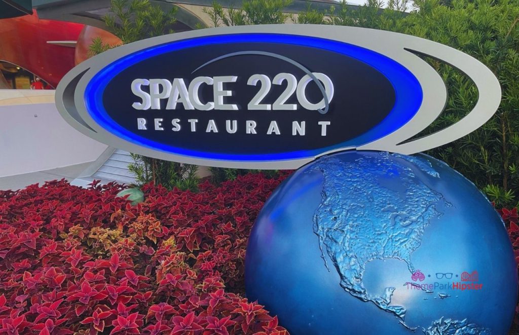 Epcot Space 220 blue and gray Restaurant sign with a blue earth sitting in a garden of flowers. Keep reading to learn more about the best things to do at Disney World for solo travelers.
