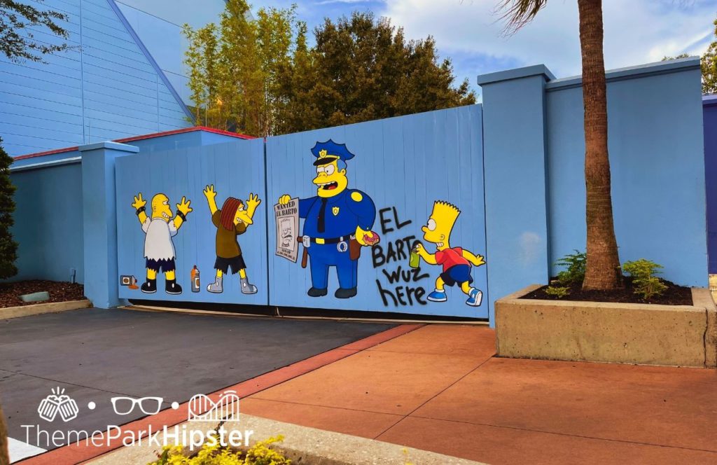 Universal Orlando Resort bart simpson spray paint on blue fence wall Simpsons Land in Universal Studios. Keep reading for the full guide to the BIG Pink Donut from Universal Lard Lad.