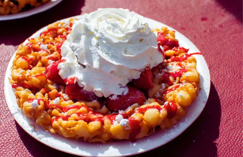 Funnel Cake topped with sugar Strawberry and Whip Cream on red table. Some of the best food at Hersheypark.