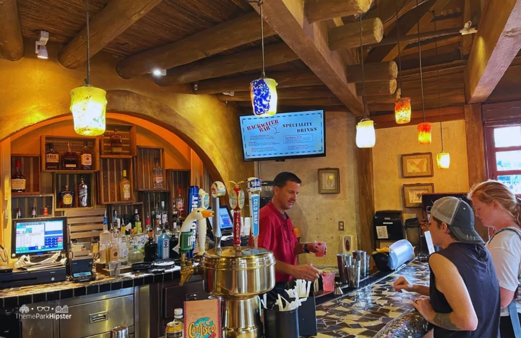 Universal Orlando Resort Backwater Bar in Confisco Grill at Islands of Adventure, with guests sitting at the bar and the bartender mixing a drink. Keep reading to find out more about the best bars at Universal Orlando.  