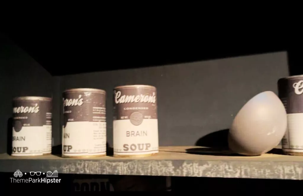 Cinema Slasher House prop display of brain soup cans and a bowl on the shelf. Keep reading to find out all you need to know about Knott’s Scary Farm mazes 2023.