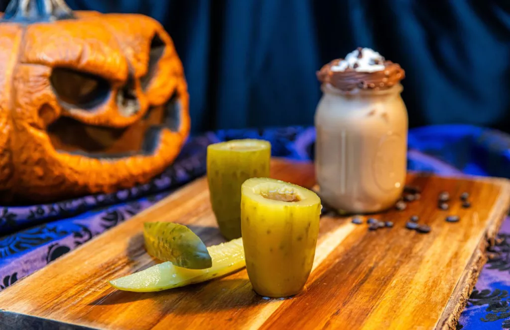 Judge Roy Bean pickle shot and chocolate milkshake at the 2023 Knott's Scary Farm at Knott's Berry Farm in California with a jack o-lantern on the table. Keep reading to learn more about Knott’s Scary Farm houses.