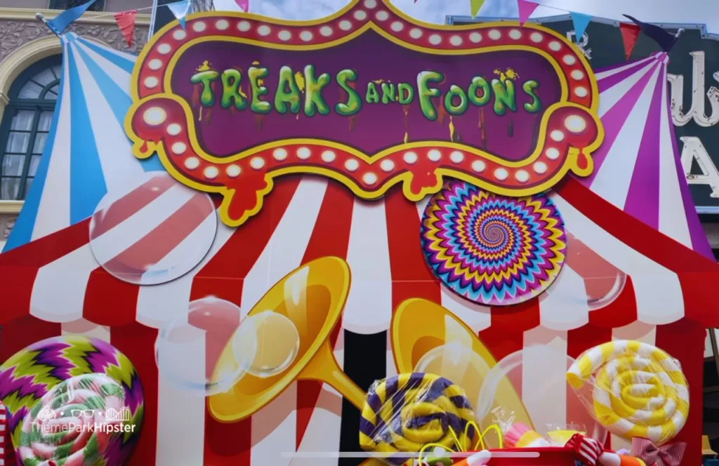 ÙTreaks and Foons sign with circus theme colors and candies at The Lights, Camera, Hacktion Eddie's Revenge HHN 30 Scare Zone at Halloween Horror Nights 2021. Keep reading to find out more about HHN scare zones.