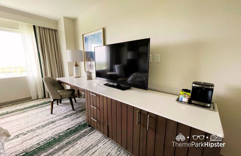 King Bedroom with desk area, flat screen tv, lamp, sitting area and big window at Hilton Signia Hotel at Disney World. Keep reading to find out more about Hilton Signia Hotel at Disney World.