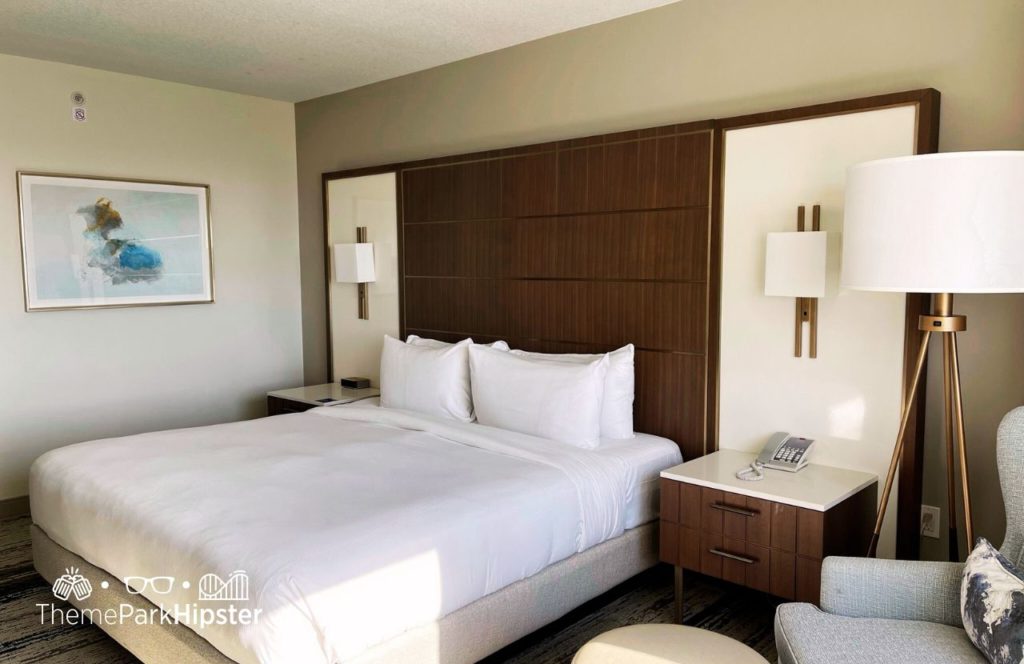 King bed room with a beautiful framed painting with lots of lamp fixtures, a sitting area and big fluffy pillows at Hilton Signia Hotel at Disney World. Keep reading to find out more about Hilton Signia Hotel at Disney World.